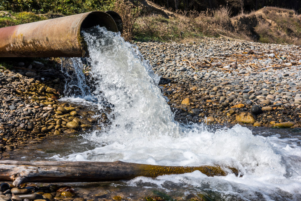 Water flowing heavily from old pipe into runoff pond