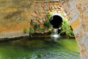 Water flows from the pipe into the river under the bridge.